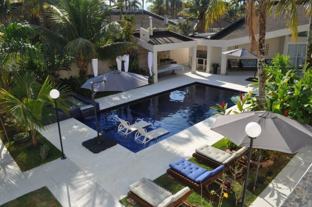 Piscina da Pousada Village Cozumel com um espaço amplo ao redor da piscina com árvores e sofás para se sentar