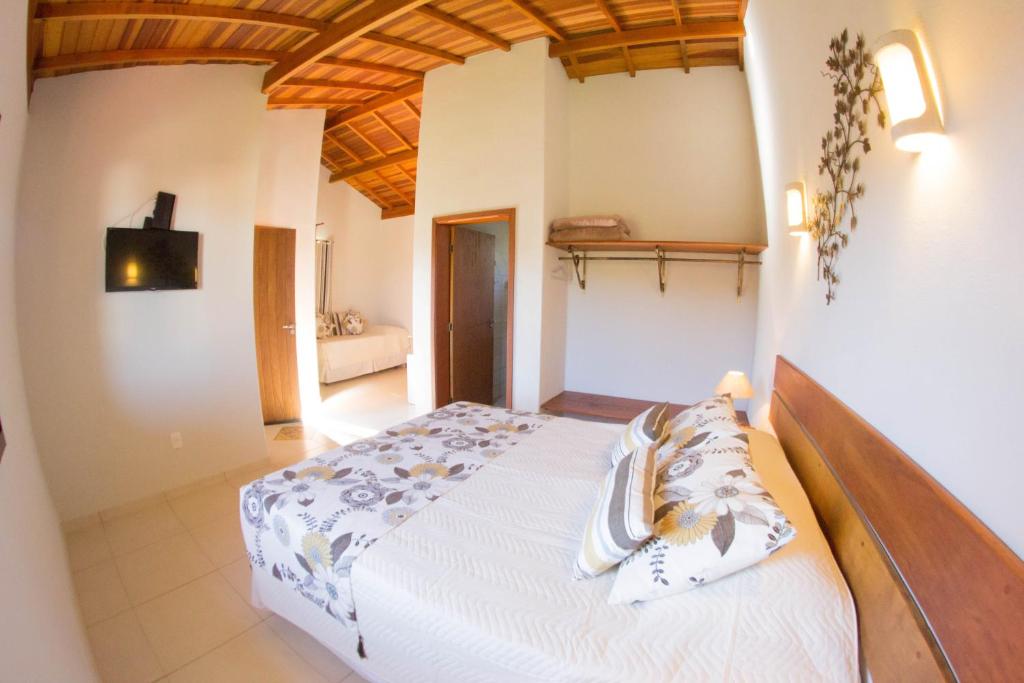 Um quarto com uma cama de casal, TV na parede, prateleiras de armário abertas e uma porta que leva a outro cômodo, na Pousada Morro Verde em Águas de Lindóia, para representar pousadas no interior de SP para casal.