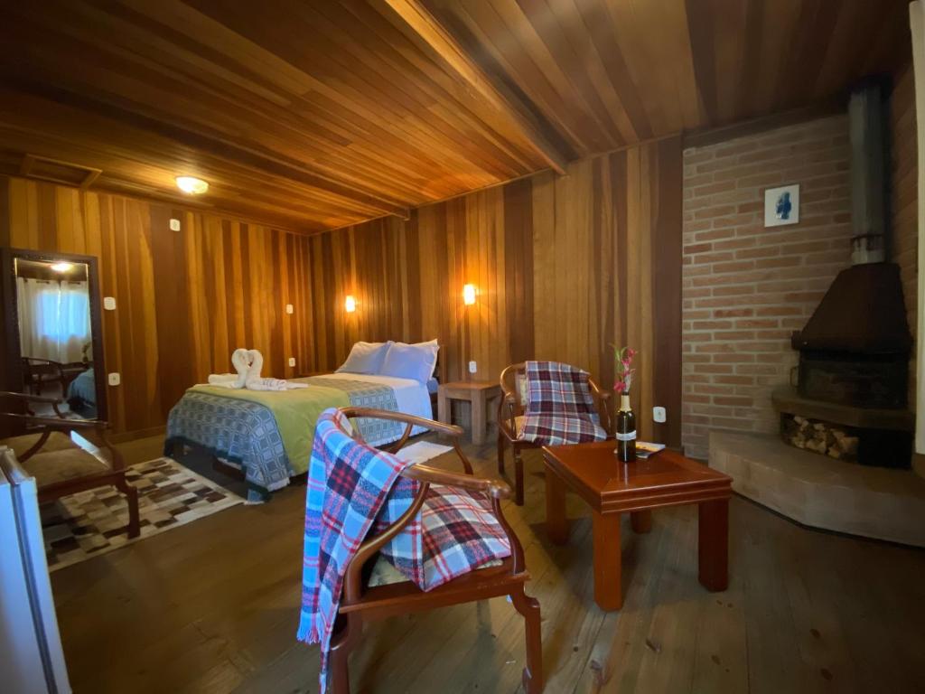 Um quarto de madeira aconchegante com uma cama de casal, duas cadeiras com cobertores xadrez, uma lareira e uma pequena mesa com vinho, na Pousada Sotaque Mineiro em Cunha, para representar pousadas no interior de SP para casal.