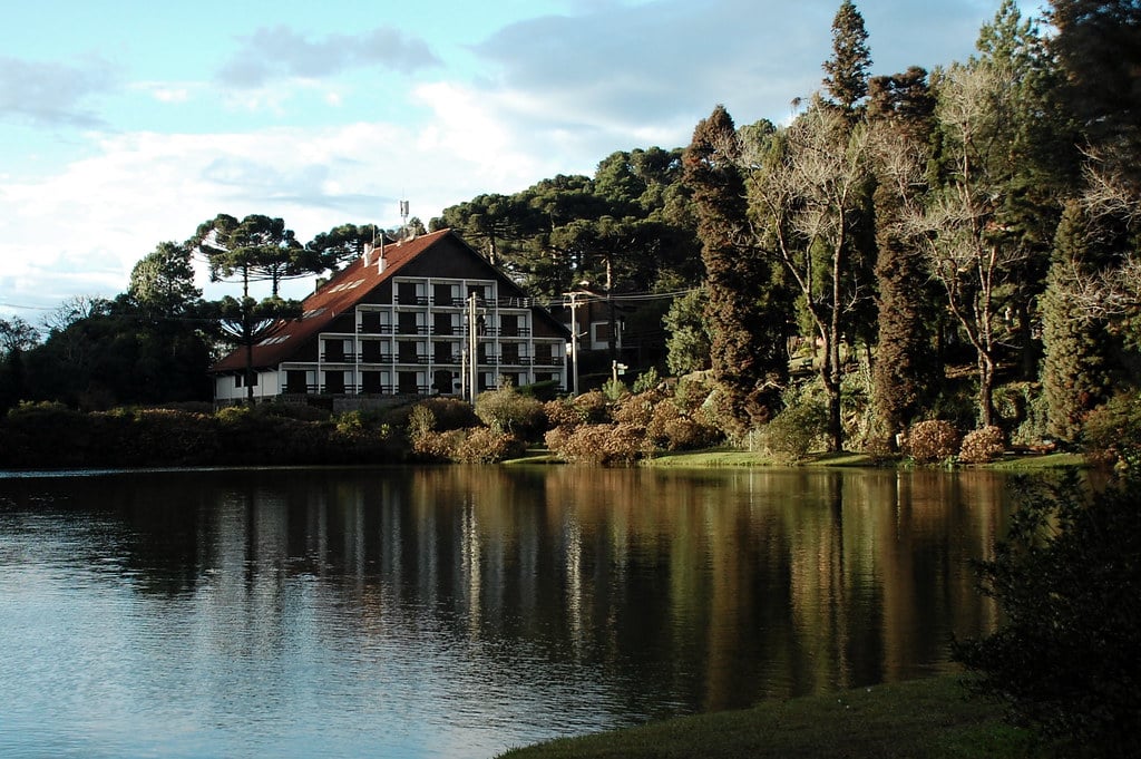 Imagem do Lago Negro em Gramado. Um lago na frente, do lado direito no fundo árvores e plantas, No meio, no fundo, uma propriedade.