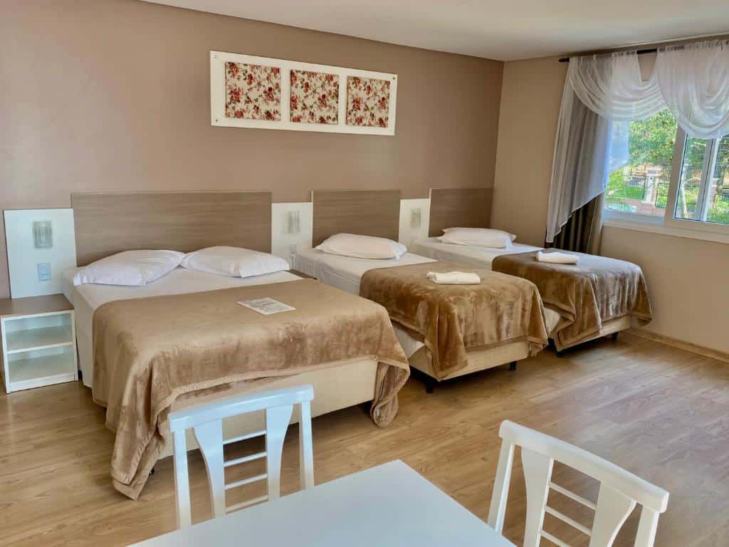Quarto da Pousada Vovô Nino. Uma cama de casal do lado esquerdo, do lado direito duas camas de solteiro e a janela do quarto. Na frente das camas uma mesa com cadeiras. Foto para ilustrar post sobre pousadas pet friendly em Gramado. Foto para ilustrar post sobre pousadas pet friendly em Gramado.