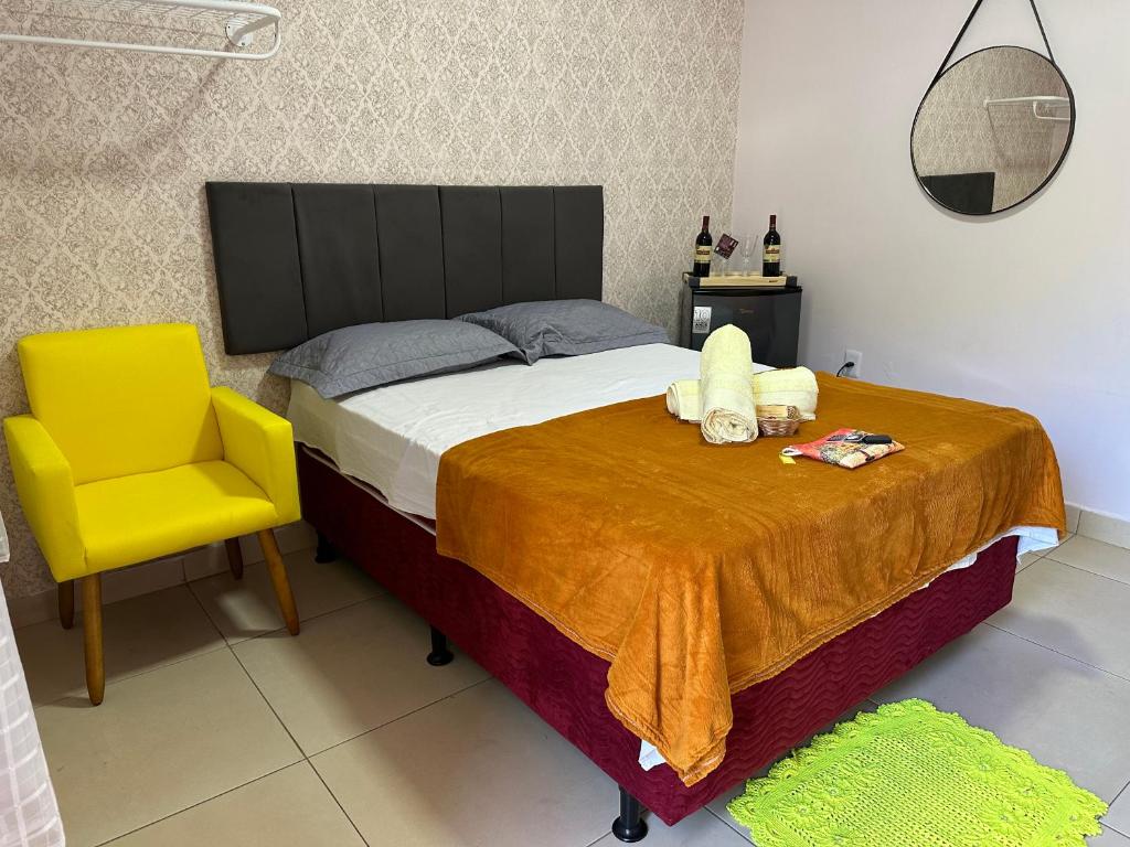 Quarto da Pousada Cantinho de Piri. Uma cama de casal está no meio, ao seu lado esquerdo uma cadeira e ao seu lado direito um figobar e um pequeno espelho redondo de parede. 