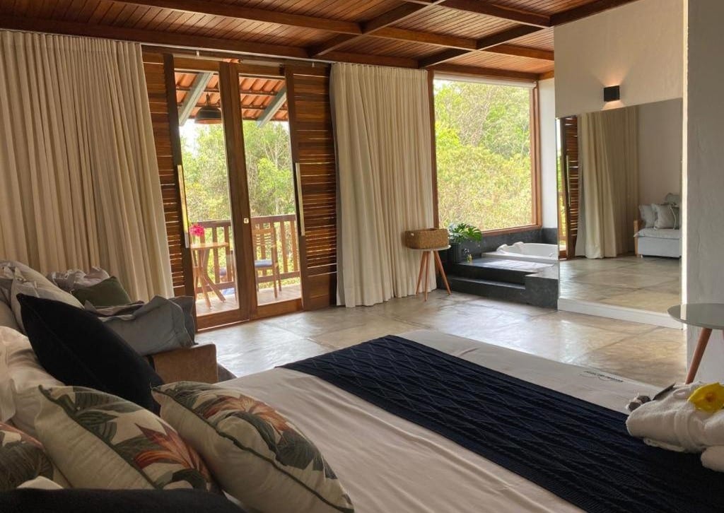 Quarto da Pousada Vereda da Serra. Uma cama de casal está no canto direito da imagem, ao lado de um sofá do lado direito. Do outro lado do quarto está um espelho e uma banheira de hidromassagem. A hospedagem é uma das pousadas pet friendly em Pirenópolis.