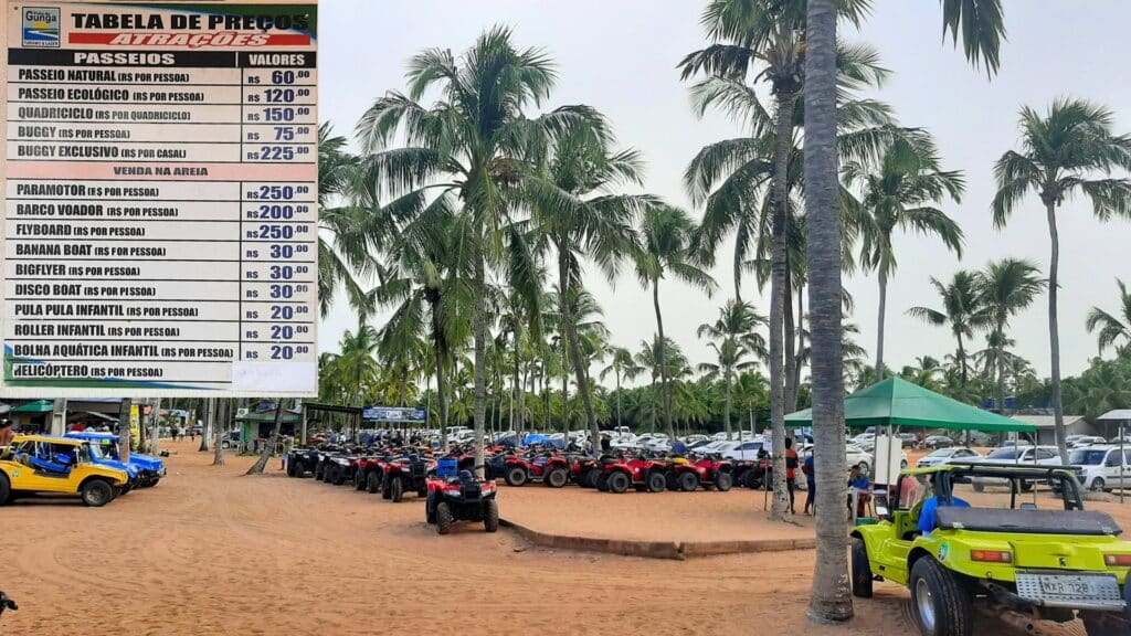Área com coqueiros e areia, com vários carros de buggy e quadriciculos estacionados