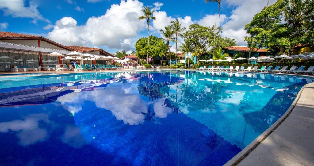 Piscina com espreguiçadeiras, cadeiras e guarda-sóis no Resort Arcobaleno em Porto Seguro