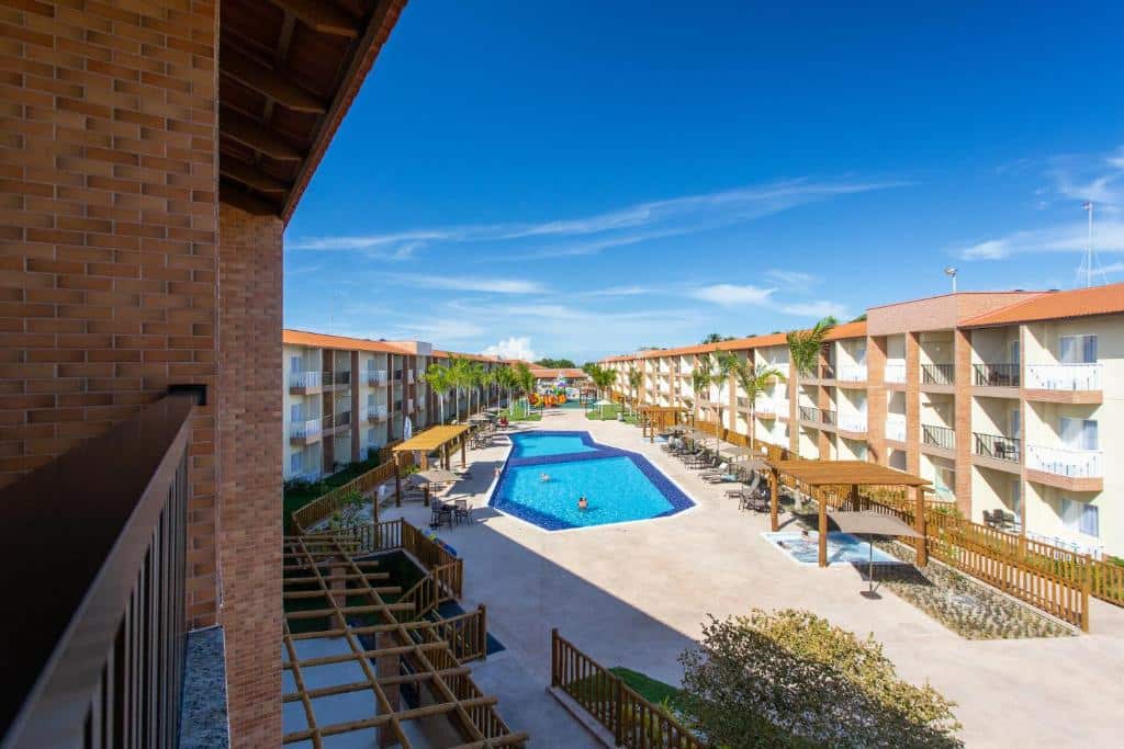 Foto da sacada de uma das unidades do Ondas Praia Resort em Porto Seguro, com vista para os demais apartamentos e uma piscina ao centro