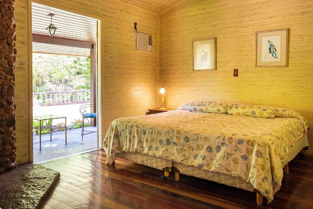 Um quarto com uma cama king-size, dois quadros emoldurados na parede e uma porta aberta para um pátio com cadeiras ao ar livre.