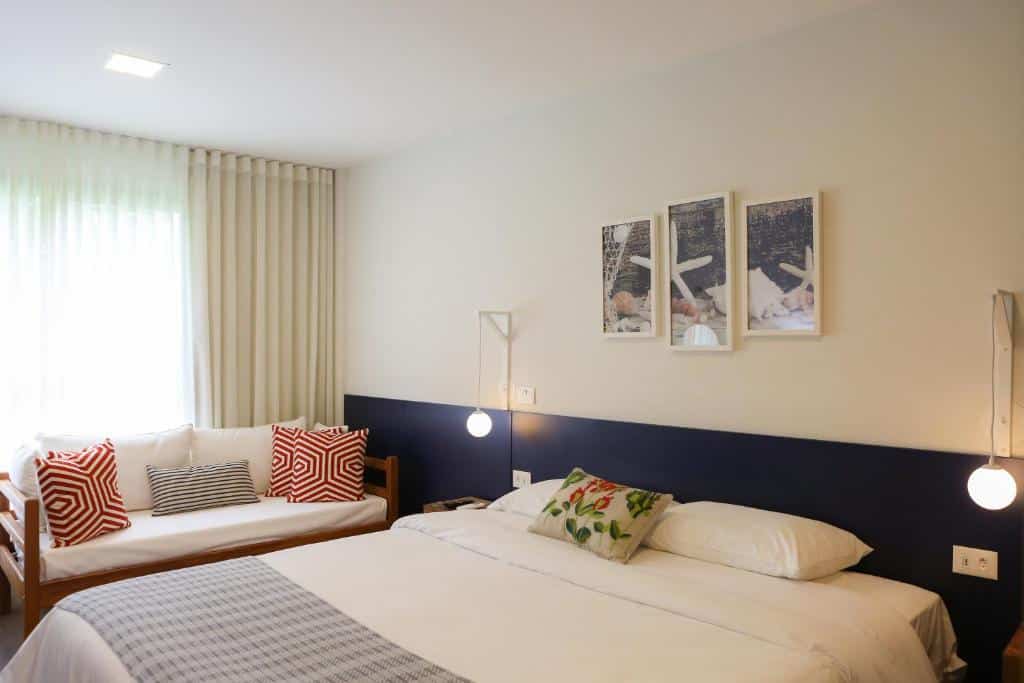 Um quarto de hotel com uma cama de casal, um sofá, travesseiros decorativos, arte na parede e duas luzes de cabeceira penduradas.