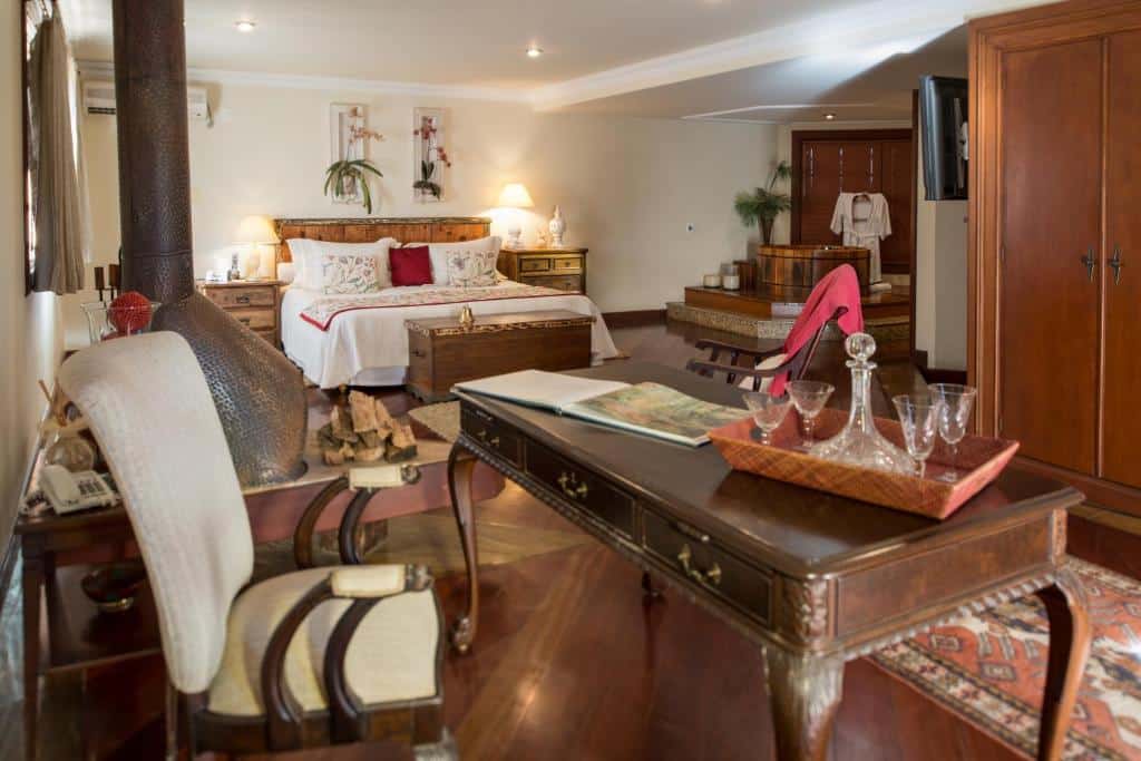 Quarto espaçoso com uma cama de casal, escrivaninha, poltrona, lareira e móveis de madeira sobre piso de madeira polida.