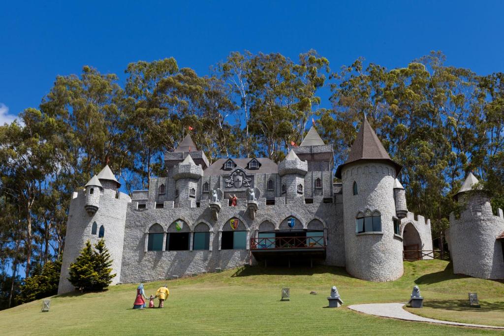 Um castelo de pedra cinza com torres fica em uma colina gramada, com pessoas vestidas como personagens de livros de histórias na frente. Um dos resorts no Rio de Janeiro.