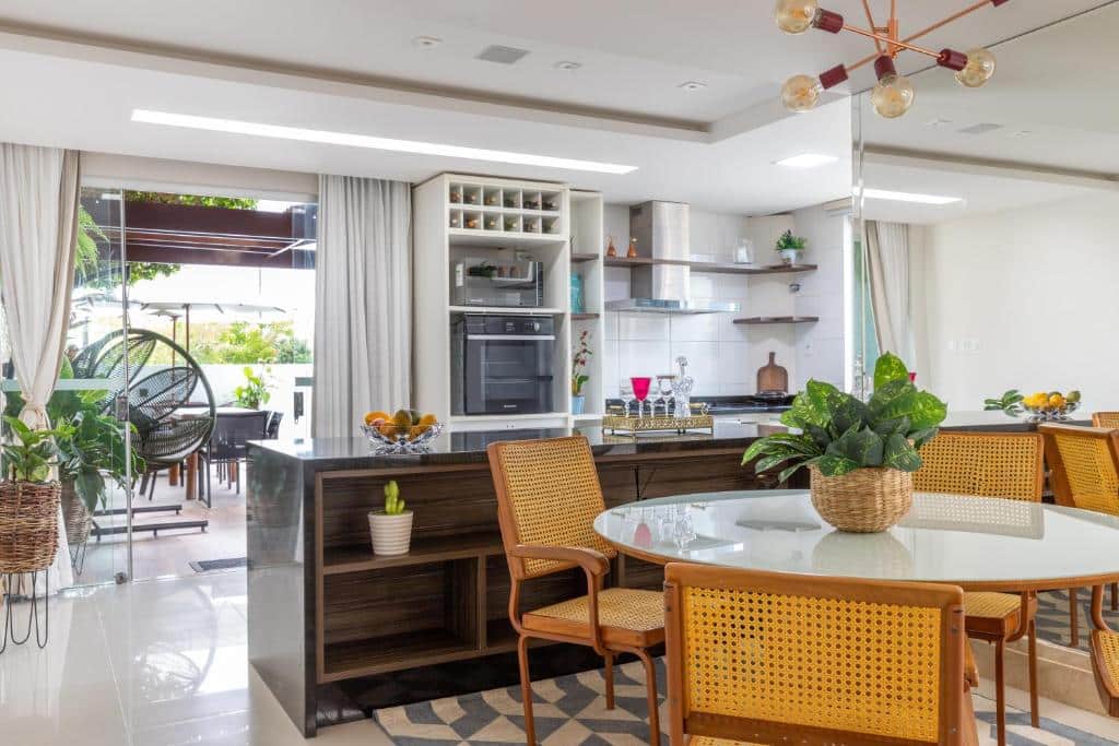 Moderna cozinha aberta e área de jantar com móveis de madeira, plantas de interior e grandes janelas que permitem a entrada de luz natural, na Casa Caju.
