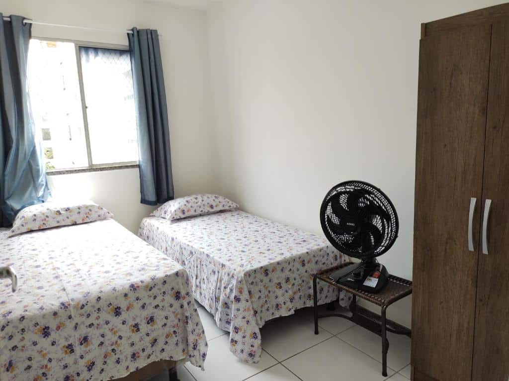 Quarto do Apartamento Condominio Caminho dos Ventos. Uma cama de casal do lado esquerdo, do lado direito uma cama de solteiro. Na frente um ventilador e um guarda-roupa. No fundo a janela. Foto para ilustrar post sobre airbnb em Aracaju.