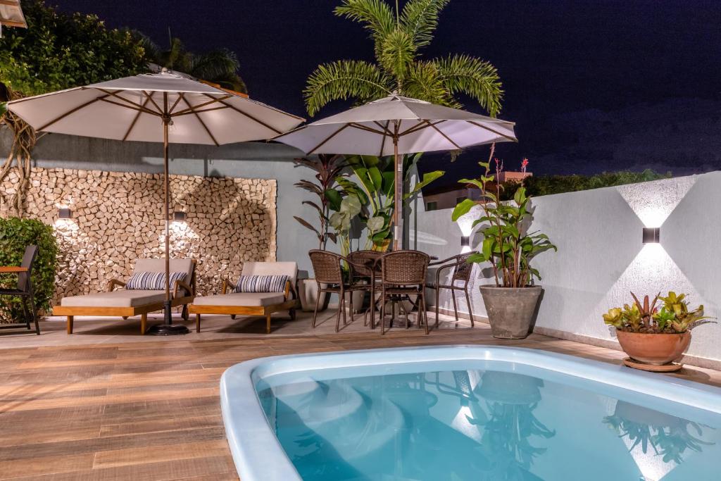 Área externa da Casa Caju. Na frente uma piscina, no fundo cadeiras de tomar sol, mesa e cadeiras com guarda-sol.
