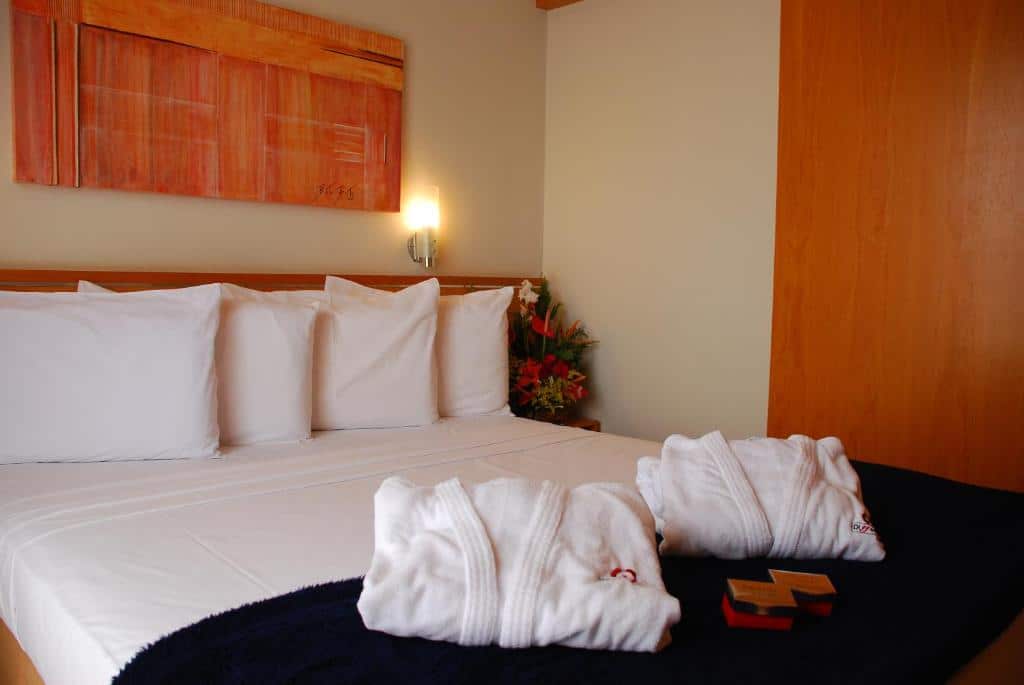 Quarto no Differential Flat. A cama é de casal e há roupas de cama em cima del. Atrás dela, na parede, tem uma luminária. Representa o post de airbnb em Belo Horizonte.
