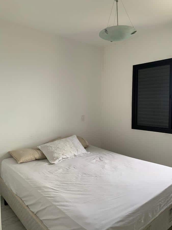Cama de casal com lençol e travesseiros na Martim de Sá de frente pro mar, um dos airbnb em Caraguatatuba. Há uma janela ao lado direito da cama.