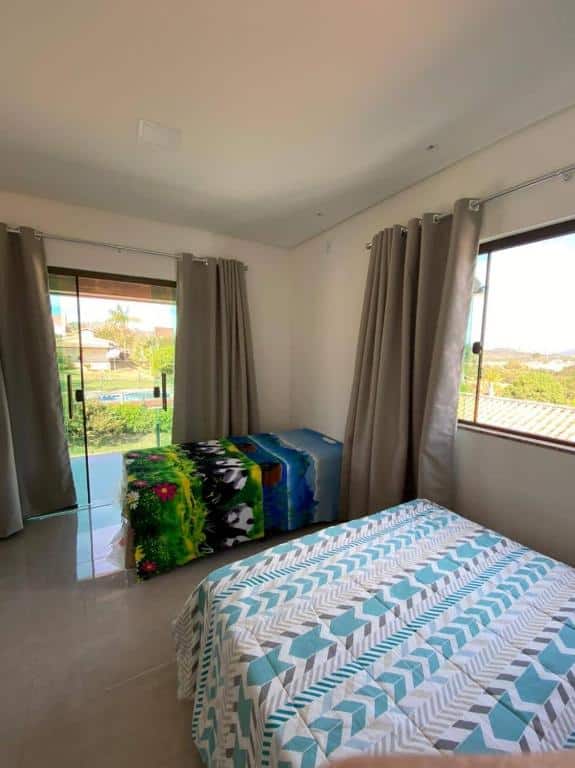 Quarto do RECANTO BRENDA com duas camas de casal meio afastadas uma da outra. No quarto há também uma janela de vidro com cortinas e uma porta de vidro com cortinas.