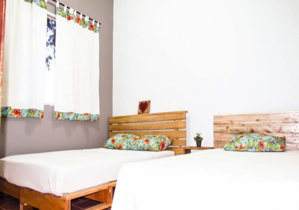 Quarto da Casa de Temporada em Capitólio com uma cama de casal e uma cama de solteiro com cabeceiras feitas de pallet de madeira. Na parede direita do lado da cama de casal tem uma janela com cortina.