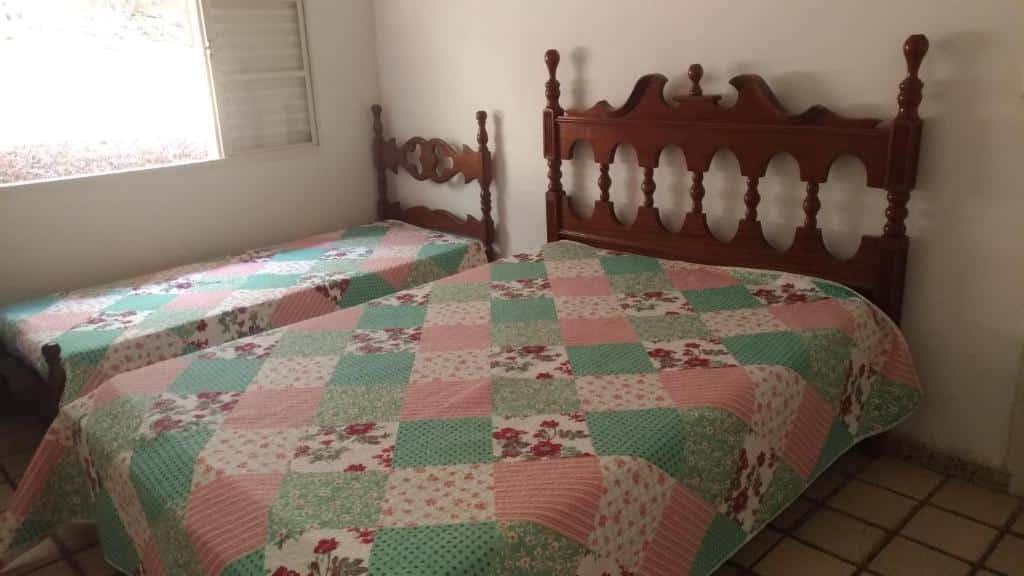 Quarto da Casa em Escarpas do Lago com uma cama de casal ao lado uma cama de solteiro. Do lado da cama de solteiro tem uma janela aberta.