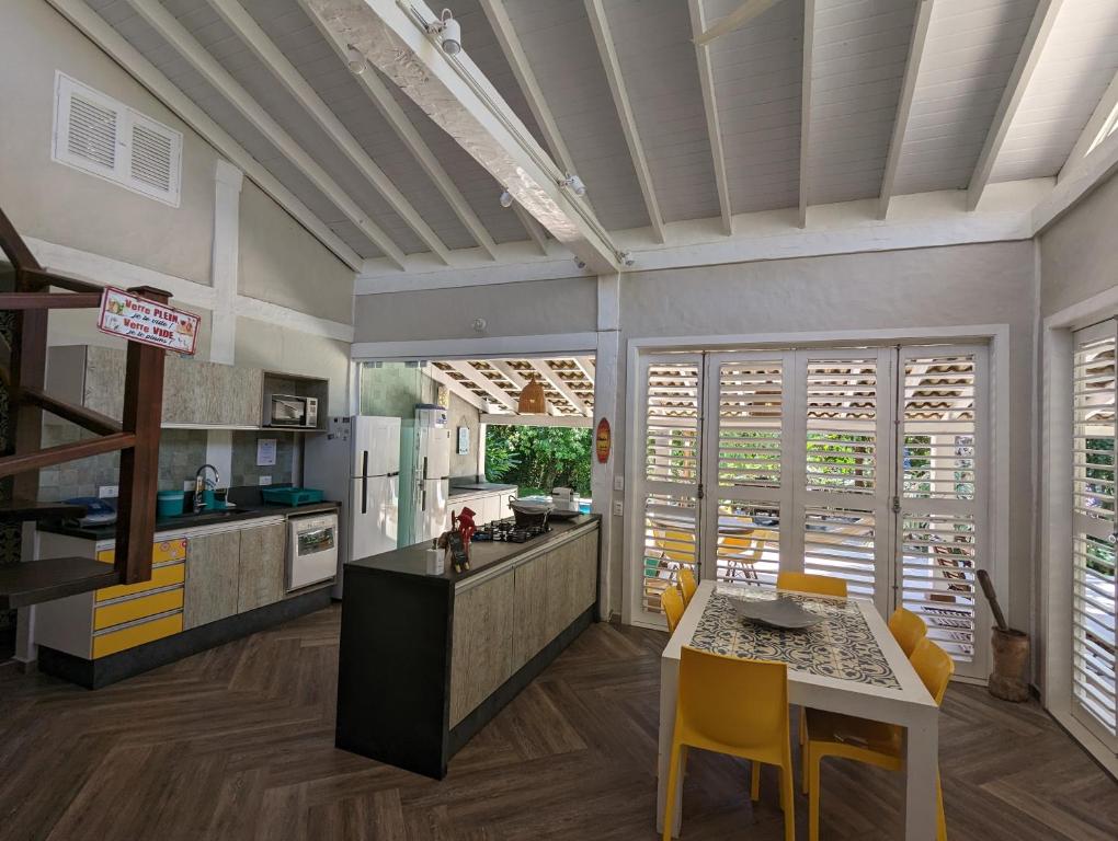 Cozinha moderna da Linda Casa Praia de Paúba em condomínio com piso de madeira, ilha, cadeiras amarelas ao redor de uma mesa de jantar e portas de vidro que se abrem para um pátio, para representar airbnb em Paúba.