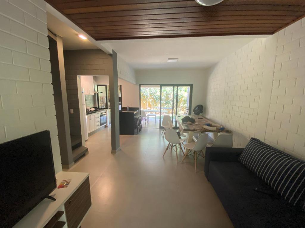 Uma sala de estar com um sofá preto, TV, mesa de jantar e vista para a cozinha e portas de vidro que levam ao exterior, na Paúba Beach House, para representar airbnb em Paúba.