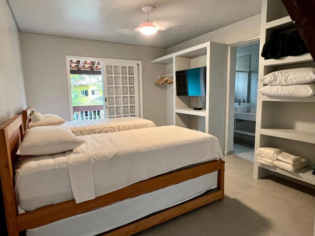 Um quarto na Casa em Paúba com duas camas de solteiro, prateleiras abertas, uma TV acoplada e vista para um banheiro adjacente, para representar airbnb em Paúba.