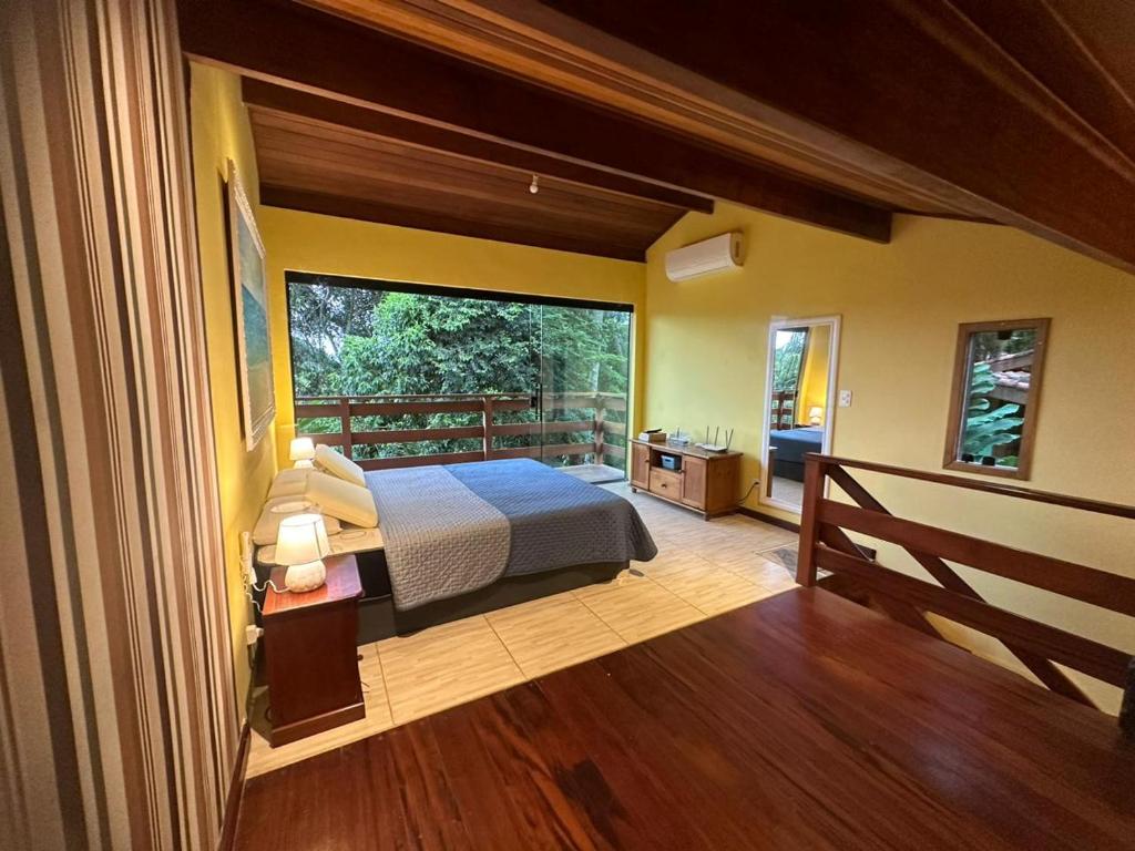 Quarto no Flat Prumirim, com cama de casal, piso de madeira, paredes amarelas, janela grande voltada para a vegetação e uma pequena área de trabalho, para representar airbnb em Prumirim.