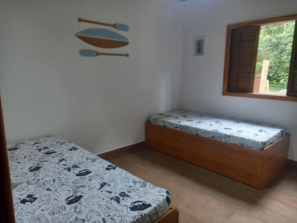 Duas camas de solteiro na Casinah mar e mato, com lençóis estampados em um quarto pequeno, uma janela à direita e arte na parede com remos acima das camas, para representar airbnb em Prumirim.