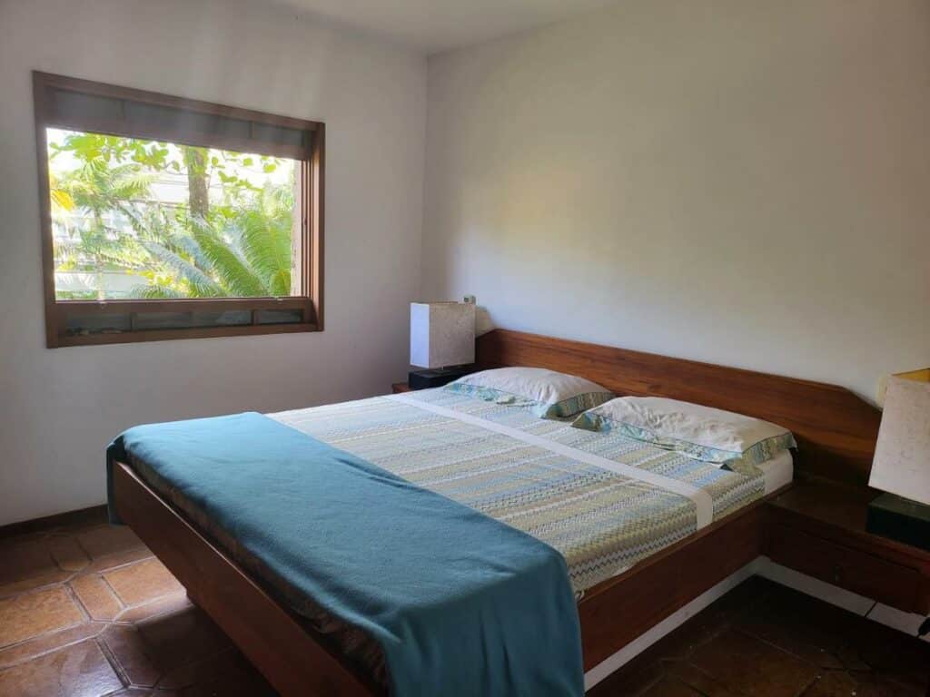 Quarto da Green Toque-Toque com cama de casal do lado direito com dias luminárias ao lado da cama em cima de uma cômoda. 