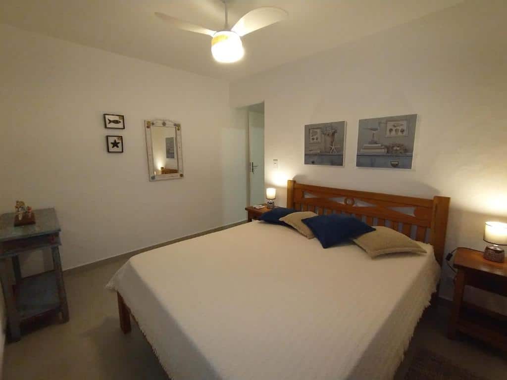 Quarto da Maré Mansa Barê com cama de casal do lado direito da imagem no centro do ambiente com uma cômoda em cada lado da cama com luminária. Representa airbnb na praia de Guaecá.