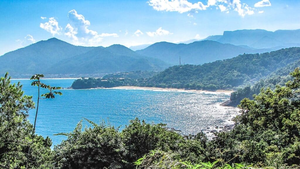 Vista geral do mar da Praia Vermelha do Centro. Ele está rodeado por uma faixa de areia e por muita vegetação. 