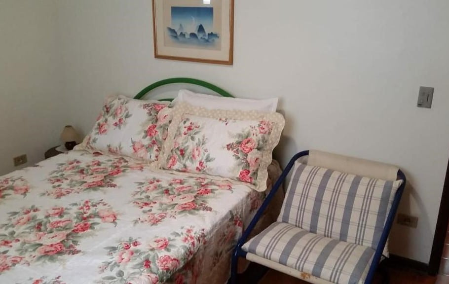 Quarto do Ubatuba Tenório apto térreo 6 pess. Uma cama de casal está ao lado de uma cadeira, para representar airbnb na Praia Vermelha do Centro.