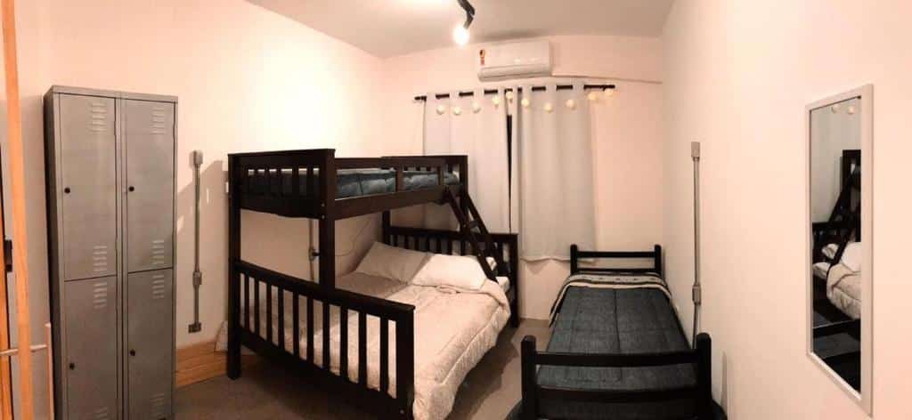 Um quarto do Imagina Hostel com um beliche, uma cama de solteiro, armários de metal, um espelho de parede e uma janela com cortinas brancas.