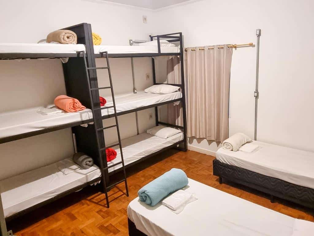 Um dormitório do Lamparina Hostel com dois beliches e uma cama de solteiro, cada um com toalhas dobradas e roupas de cama bem arrumadas.