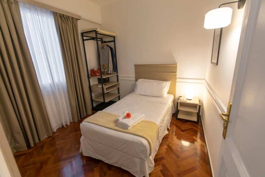 quarto do El Misti Hotel Buenos Aires Centro com cama de solteiro, mesinha e luminária de apenas um lado, guarda-roupa aberto com espaço para calçados e cabides, além de uma janela com cortinas