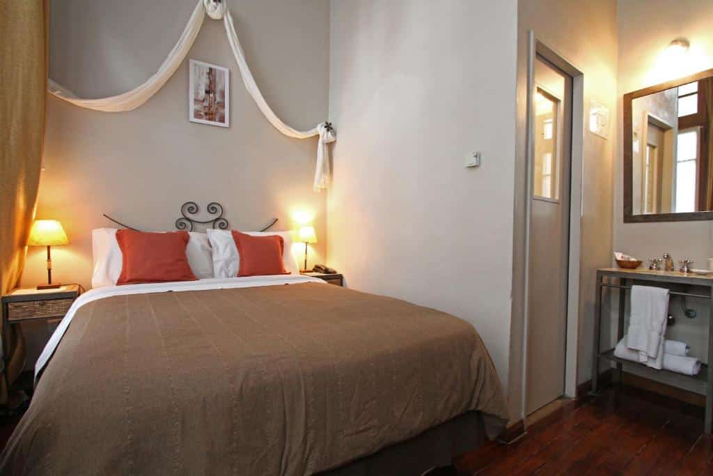 quarto do A Hotel com em espaço bacana, cama de casal com luminária e mesinha de ambos os lados, com janela de um lado e outro, lavabo 
