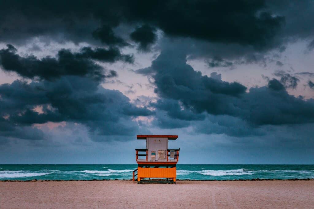 Imagem da praia de Miami no final do dia com areia a frente no centro uma casinha de madeira e ao fundo o mar.