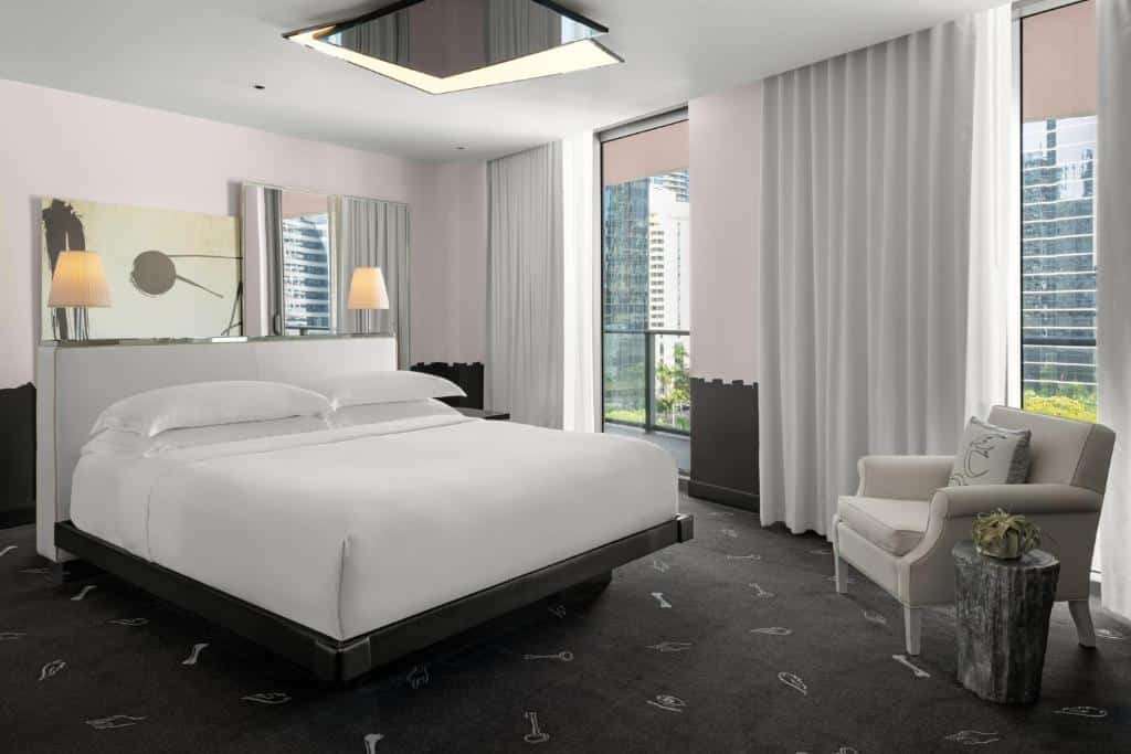 Quarto do DUA Miami, Autograph Collection  com cama de casal do lado esquerdo da imagem no centro em frente a cama do lado esquerdo uma poltrona. Representa hotéis 5 Estrelas em Miami.