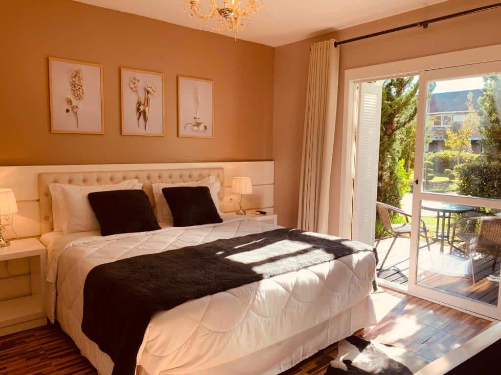 Quarto da Pousada Quinta do Vale. No lado esquerdo, uma cama de casal com uma mesa e um abajur de cada lado. No lado direito, a porta da varanda com uma mesa e duas cadeiras e um jardim.