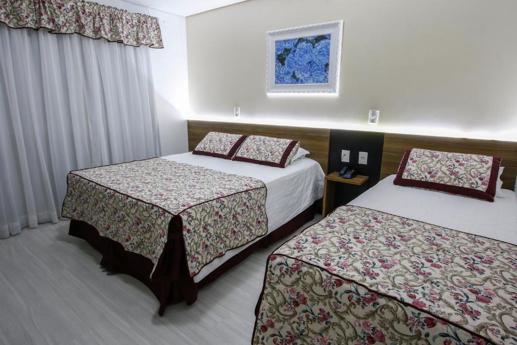 Quarto do Sky Premium Hotel Gramado. Uma cama de casal e uma cama de solteiro do lado direito, entre elas uma mesa com telefone. Do lado esquerdo uma cortina fechada. Foto para ilustrar post sobre hotéis baratos em Gramado.