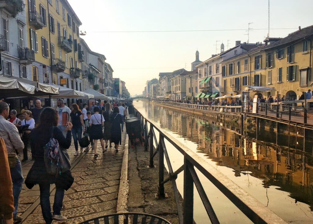 Um canal no bairro Navigli com muitas pessoas caminhando pelas margens do local com diversos locais para comer