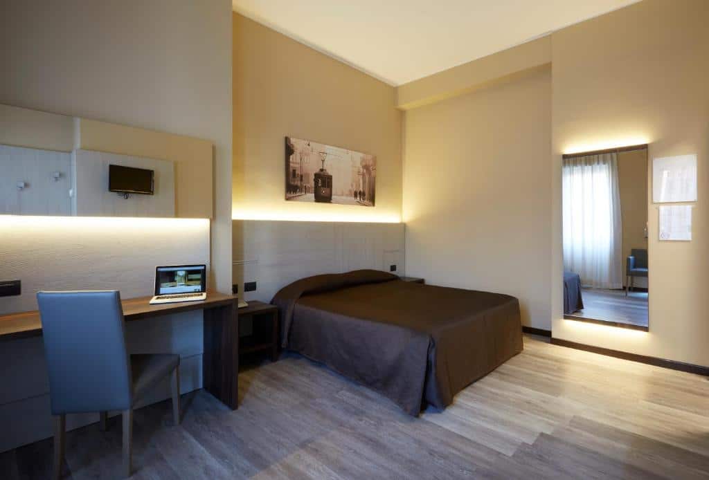 Quarto do Hotel Ritter com uma cama de casal, um espelho, uma mesa de escritório com uma cadeira, o ambiente é espaçoso, para representar hotéis baratos em Milão