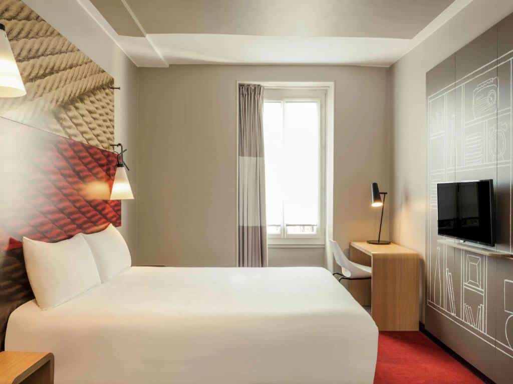 Quarto moderno do ibis Paris Avenue de la Republique com uma cama de casal, arte na parede, escrivaninha, cadeira, janela com cortina e uma TV na parede.