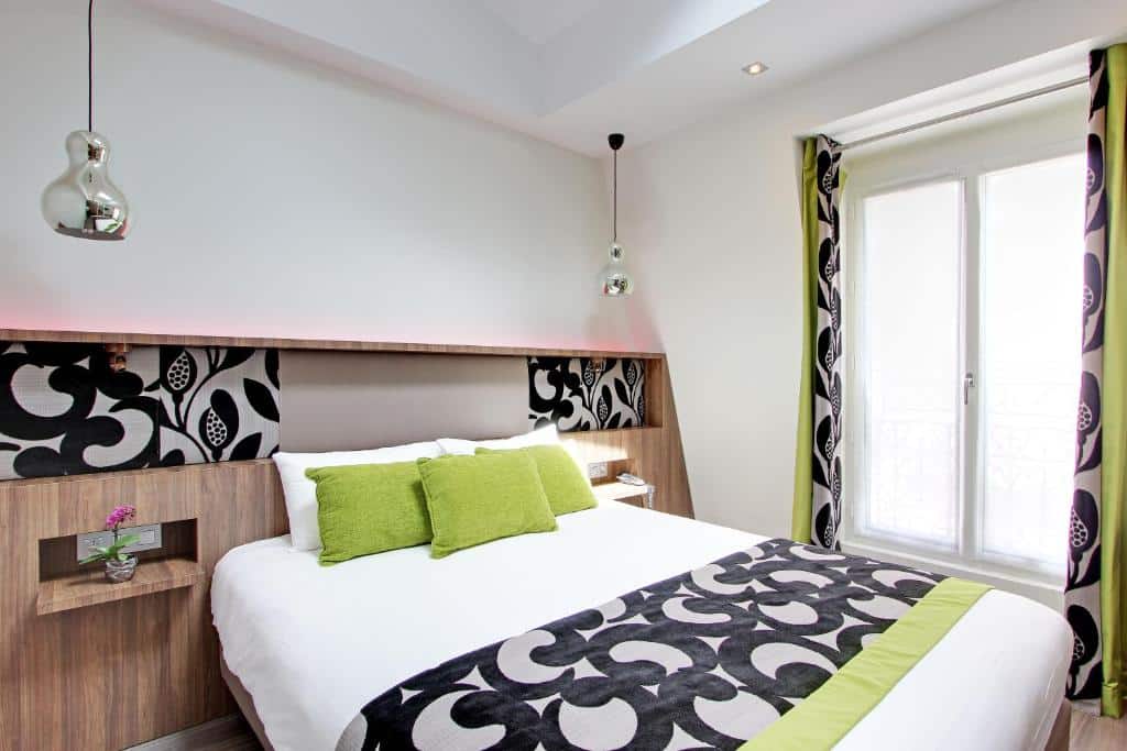 Quarto moderno do Hotel Alhambra com uma cama de casal, dois travesseiros verdes, roupa de cama estampada, prateleiras de cabeceira e luzes pendentes.