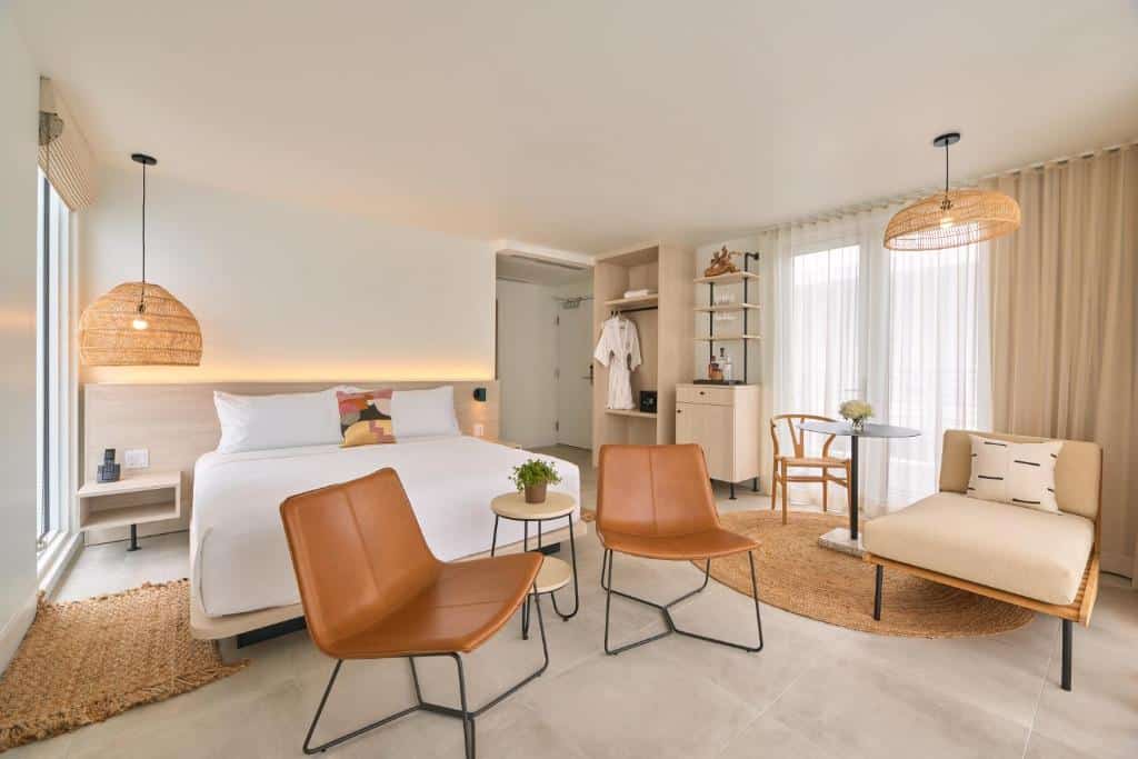 Quarto do Hotel Greystone – Adults Only com duas cadeiras a frente do lado direito uma poltrona e ao fundo uma mesa redonda com cadeira. Atrás das duas cadeiras uma cama de casal. Representa hotéis boutique em Miami.