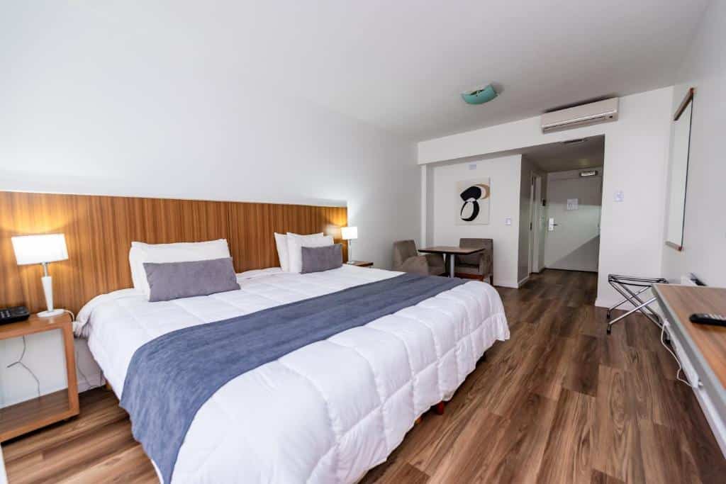 quarto do Hotel Bys Palermo com cama extra grande, com mesinha dos lados com luminárias, tv em frente, ar-condicionado em um ambiente amplo e arejado