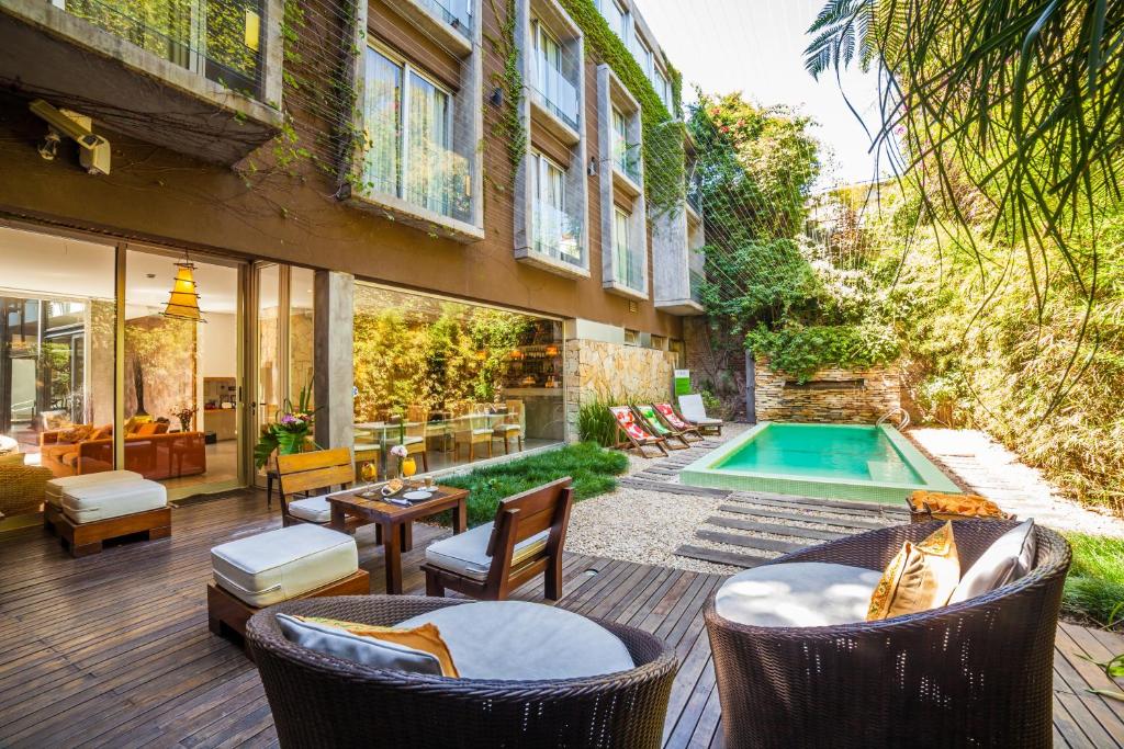 área externa do Mine Hotel, um dos hotéis românticos em Buenos Aires, com piscina, fachada charmosa, mesa com cadeiras e poltronas estofadas, com árvores ao redor