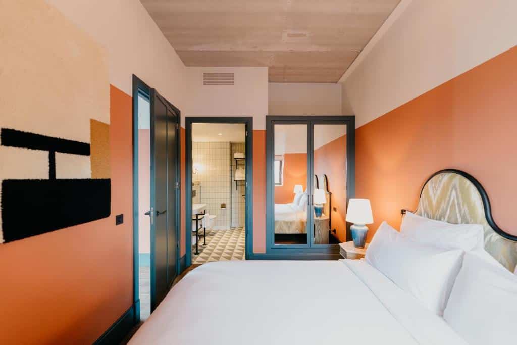 Um quarto de Hotel BOAT & CO moderno com uma parede laranja e bege, uma cama, duas portas e um banheiro com piso de azulejos. Ilustra o post de hotéis em Amsterdam