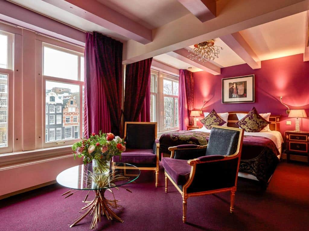 Quarto do Ambassade Hotel com paredes, carpete e cortinas roxas, uma cama de casal, cadeiras, uma mesa de vidro com flores e janelas grandes. Ilustra o post de hotéis em Amsterdam.