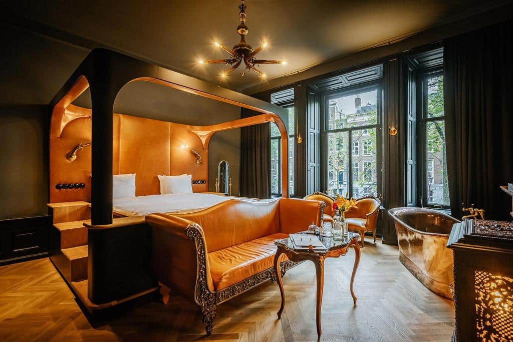 Quarto luxuoso do Boutique Hotel The Noblemen com cama de dossel, sofá ornamentado, banheira de metal, janelas grandes e piso de madeira em espinha. Ilustra o post de hotéis em Amsterdam.