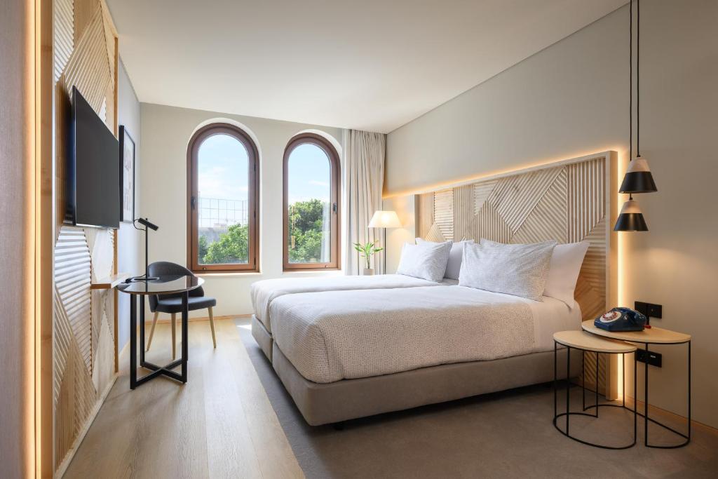Quarto moderno no INNSiDE by Meliá Braga Centro com uma cama grande, TV na parede, escrivaninha, janelas redondas e mesas de cabeceira com luminárias, para representar hotéis em Braga.